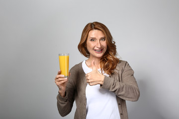 Mature woman with glass of fresh juice on grey background