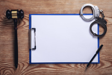  Clipboard, handcuffs, pen with judge gavel on wooden background.