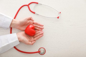 Cardiologist with red heart and stethoscope at table