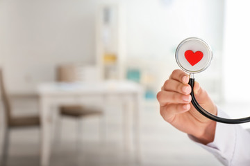 Cardiologist holding stethoscope with red heart in clinic, closeup