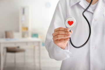 Cardiologist holding stethoscope with red heart in clinic, closeup