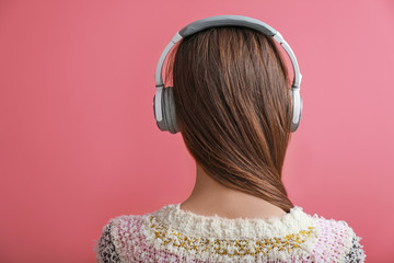 Young woman with headphones listening to music on color background
