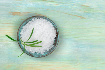 A bowl of rosemary infused sea salt, shot from above on a teal blue background with a place for text