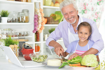 Senior man with granddaughter preparing dinner in kitchen