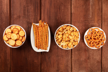 Salty crackers, sticks, pretzels, and goldfishes, shot from the top on a dark wooden background with copy space. Party snacks mix with a place for text