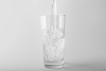Pouring of water into glass on light background