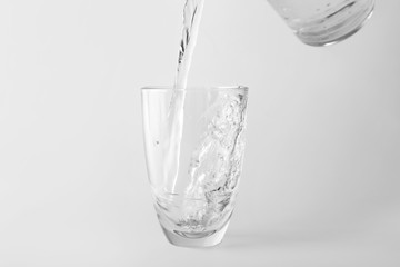 Pouring of water into glass on light background