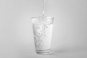 Pouring of water into glass on light background