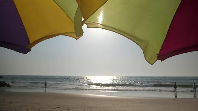 POV of a tourist lying down at the sun bench and watching Foreign & local tourists enjoying Arabian sea waves and the beach at the popular tourist and traveller destination of Goa in western Indian