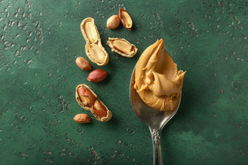 Spoon with tasty peanut butter on color background