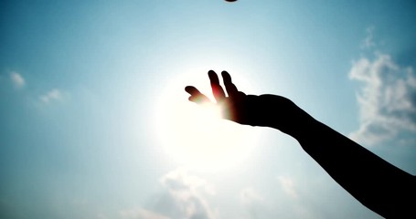Silhouette of Man's hand throwing a ball to blue sky background,