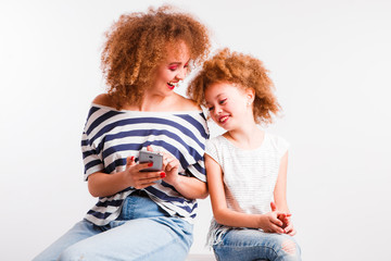 Mom and daughter with natural small curls on the head on a light background.