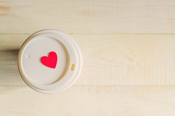 disposable craft paper coffee cup and red wooden heart on a cap. Coff to go on wooden table