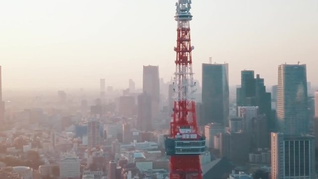 HD drone aerial above Tokyo City panning around the iconic red Tokyo Tower surrounded by tall skyscrapers during a stunning sunset with blue and orange skies