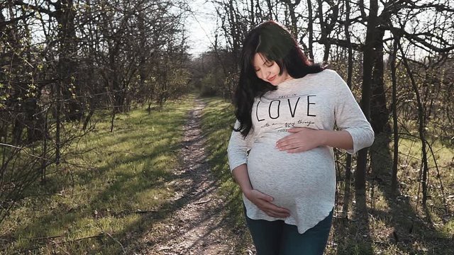 A young pregnant woman walks her fingers over the stomach. A happy pregnant woman thinks about future motherhood in the forest. Woman at 36 weeks gestation (9 months).