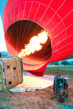 Hot air balloon with flame and basket lying on the ground on the field while filling with air and preparing to take off.