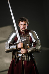 Medieval man knight in armor and weapon on dark background. Portrait of the knight