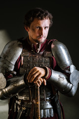 Medieval man knight in armor and weapon on dark background. Portrait of the knight
