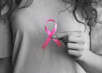 Woman’s hands holding pink ribbon, breast cancer awareness month, concept of health.