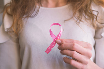 Woman’s hands holding pink ribbon, breast cancer awareness month, concept of health.