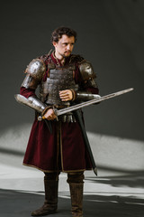 Medieval man knight in armor and weapon on dark background. Portrait of the knight