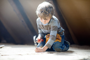 Little kid boy helping with toy tools on construction site. Funny child of 6 years having fun on building new family home. Kid with nails and hammer helping father to renovate old house.