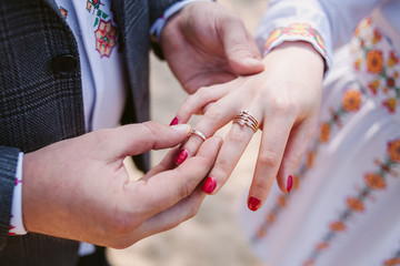 Fototapeta premium The groom wears the bride a wedding ring at the ceremony. Bride and groom in the national Ukrainian clothes.