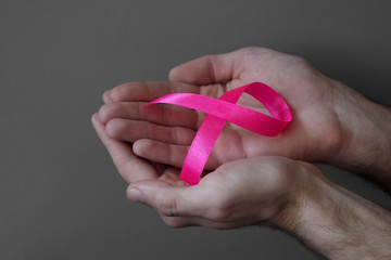Man’s hands holding pink ribbon, breast cancer awareness month, concept of health.