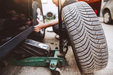Auto mechanic changing tire while crouching at workshop. Selective focus on tire.