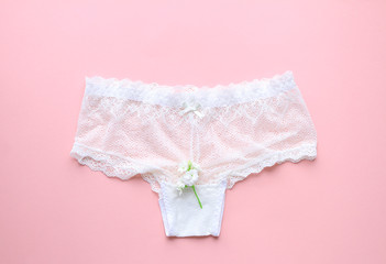 White sexy lace women's panties and white flowers on pink background.Top view.