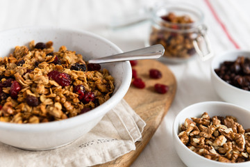 Bowl of homemade granola with nuts and fruits on white linen background. Side view, copy space. Healthy breakfast concept