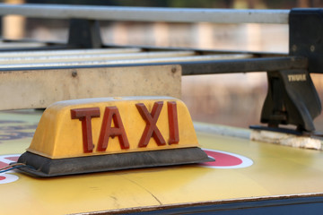 Taxi light sign or cab sign in drab yellow color with red text on the car roof.