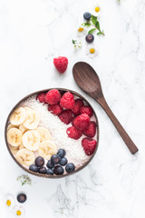 Healthy breakfast bowl. Banana smoothie bowl with coconut flakes, banana slices, raspberry and blueberry. Top view, flat lay
