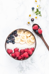 Healthy breakfast bowl. Banana smoothie bowl with coconut flakes, banana slices, raspberry and blueberry. Top view, flat lay