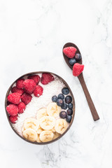Healthy breakfast bowl. Banana smoothie bowl with coconut flakes, banana slices, raspberry and blueberry. Top view, flat lay