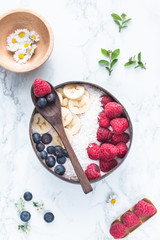 Healthy breakfast bowl. Banana smoothie bowl with coconut flakes, banana slices, raspberry and blueberry. Top view, flat lay