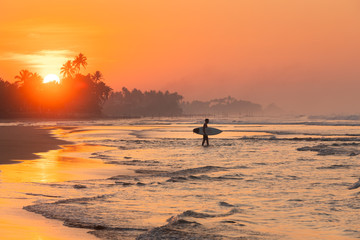 Silhouette of a surfer walking to the ocean during sunset