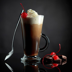 Layered coffee cocktail with whipped cream, cherry and pieces of chocolate.