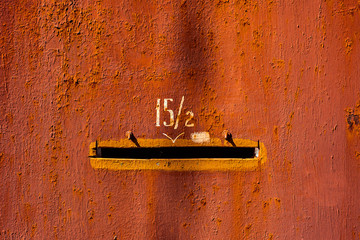 Close-up old red painted metal door with number fifteen fractions two and mail hole. Horizontal...