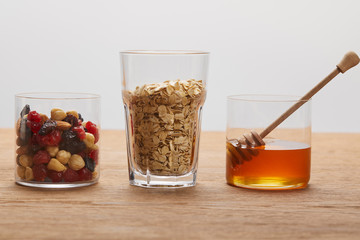 glasses with dried berries, nuts, oat flakes and honey on wooden table isolated on grey