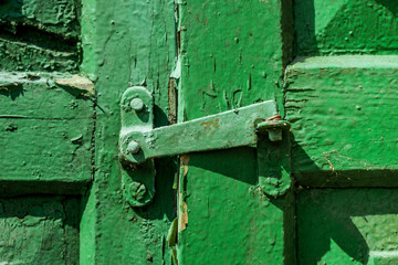 Green metal latch on wood green shutter cracked and scratch. Horizontal texture