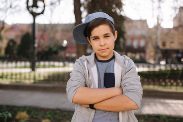 Fototapeta premium Stylish little school boy in blue cap posing outside for photo. Boy walking in the city in sping summer weather