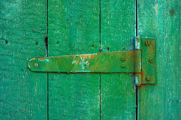 Green shabby door hinge on old green wood door with cracked and scratch. Close-up horizontal texture