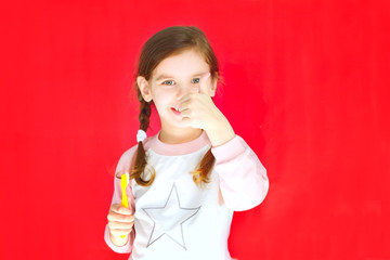 Little cute girl with a toothbrush and the location of the teeth in her hand on the red .Concept of health, oral hygiene, people and beauty. Location of the space. Selective focus.