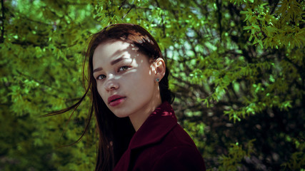 Fashionable girl with green eyes on against the background of a blossoming tree and soft light.