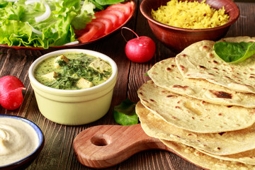 Indian vegetarian chapati cakes with vegetables, rice and hummus on a wooden table
