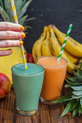Woman's hand holding glass of smoothie with straws on wooden background. Healthy summer drink