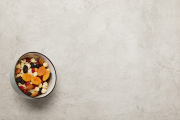 top view of bowl with muesli, dried apricots and berries, nuts on textured grey surface