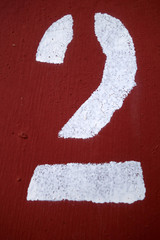 Red color number 2 in stencil on metal wall.