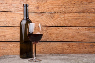 A bottle of wine, near a glass half filled with wine on wooden background